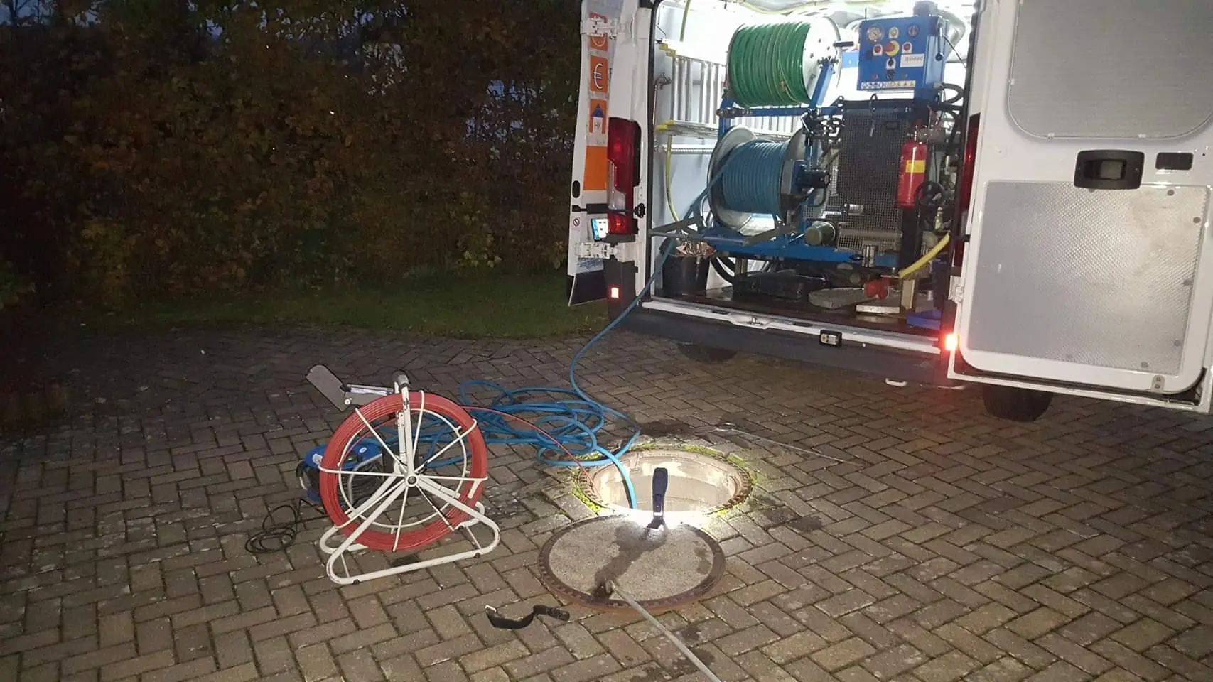 Firmenwagen mit Spültechnik am Abend, daneben ein beleuchteter offener Schacht