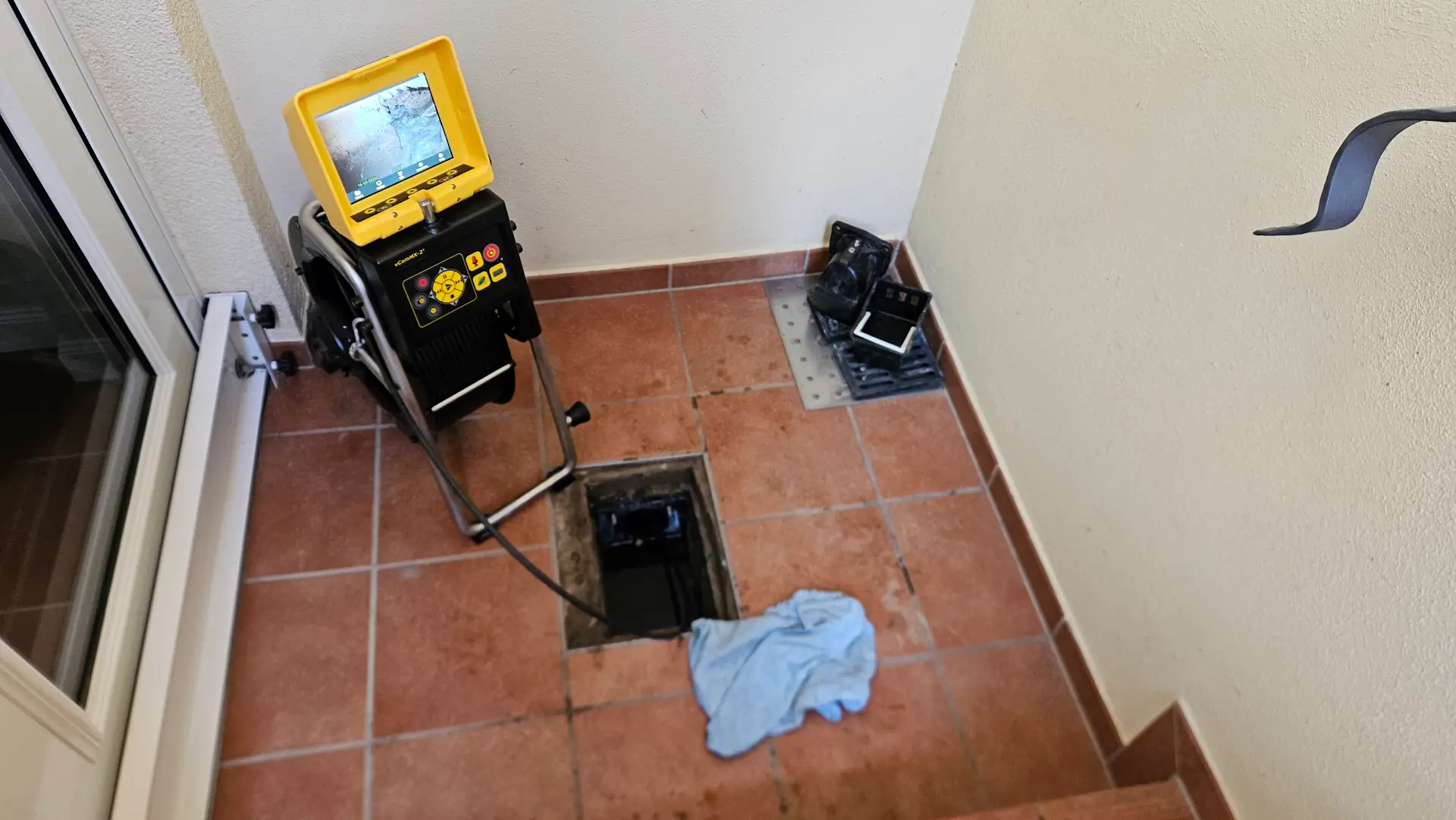 Kanalkamera an einem geöffneten Bodenablauf im gefliesten Hauseingang, ein Tuch liegt darunter