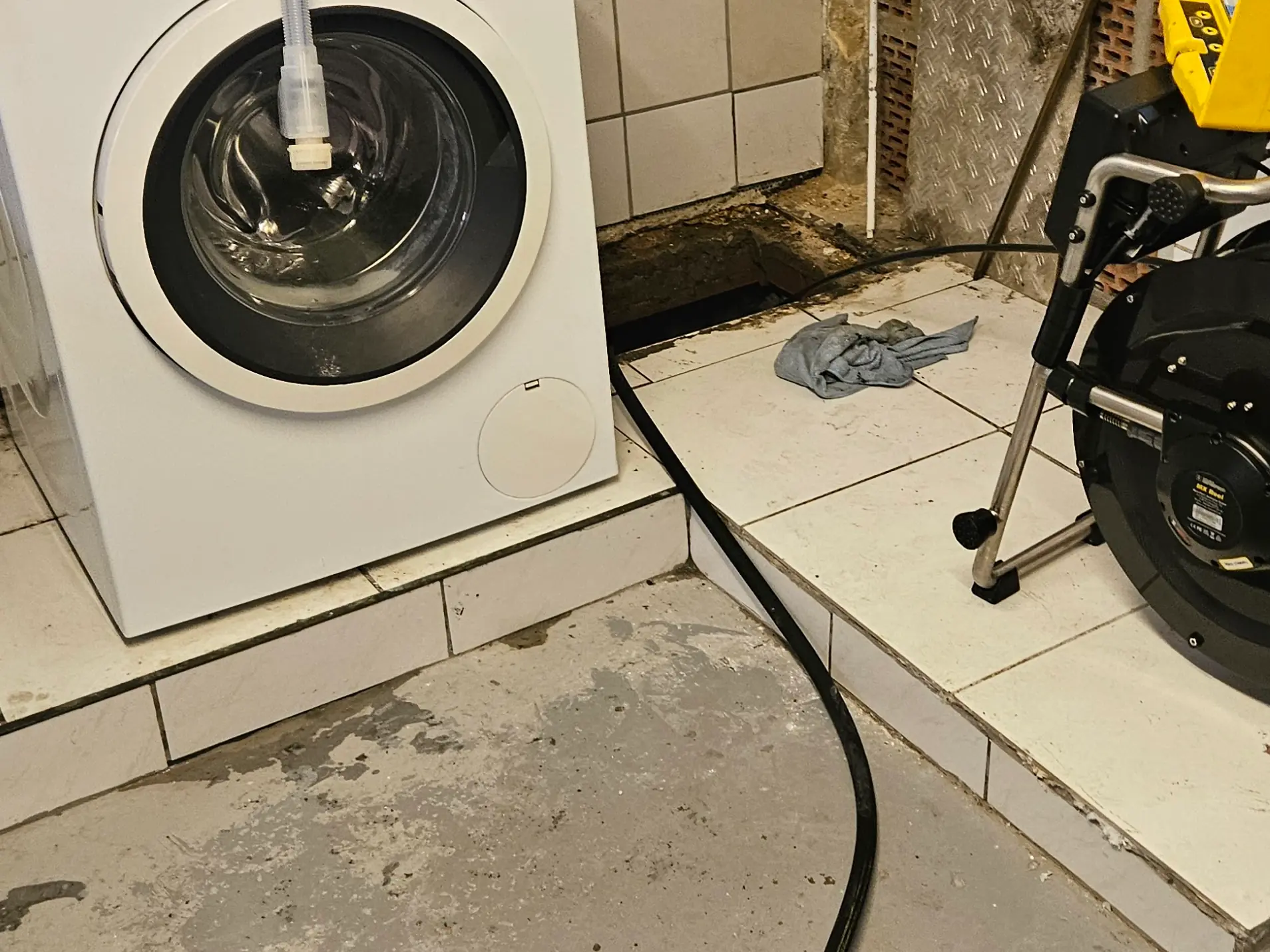 Kanalkamera neben der Waschmaschine an einem geöffneten Bodenablauf im Waschkeller