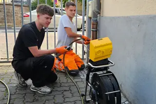 Zwei Mitarbeiter führen eine Kanalkamera in eine Leitung ein